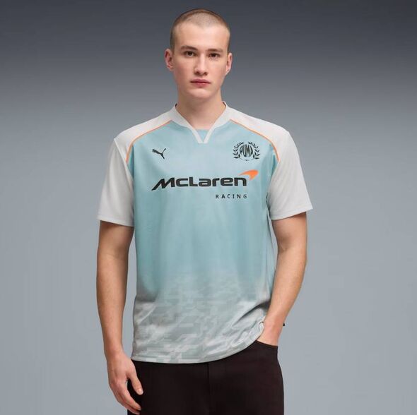 Un individu se tient sur un fond gris, portant un maillot de sport bleu clair et blanc avec le mot 