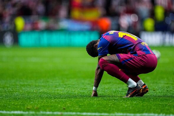 Un footballeur, vêtu d'un maillot bleu et rouge, est agenouillé sur un terrain vert, semblant plongé dans un moment de contemplation. 