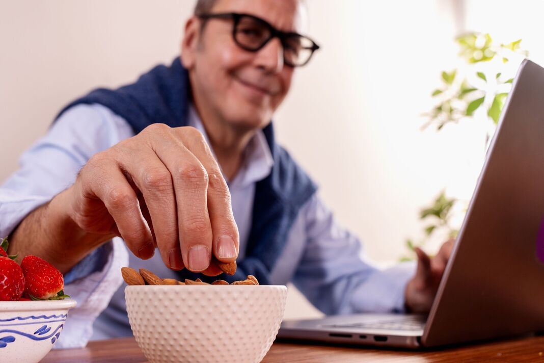 Homme âgé mangeant des amandes tout en travaillant sur un ordinateur portable, des collations saines Homme âgé mangeant des amandes tout en travaillant sur un ordinateur portable, des collations saines